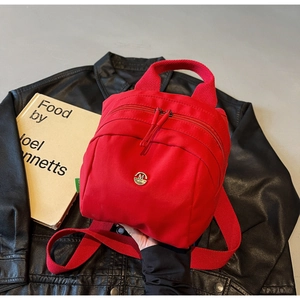 Detail shot of a red canvas mini shell bag with a metal logo on a black leather jacket
