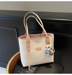 Detail of off-white pebble grain tote bag with pink straps and a cute teddy bear charm