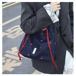 Close-up of blue denim bucket bag with cherry embroidery and red rope handle detail