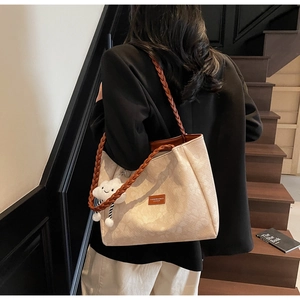 Detail of beige tote bag with woven brown strap and white cloud pendant on black stairs