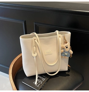 Detail of off-white lychee grain tote bag with bear charm on a black leather chair