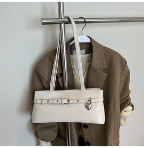 Close-up of cream underarm bag featuring a metallic heart pendant and buckle detail