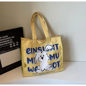 Close-up of yellow canvas tote bag featuring white cartoon rabbit and artistic blue text