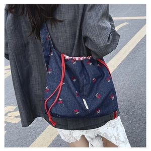 Denim bucket bag with cherry embroidery shown on model in street style setting