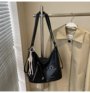 Detail of black leather tote bag with buckle pocket and woven tassel charm hanging