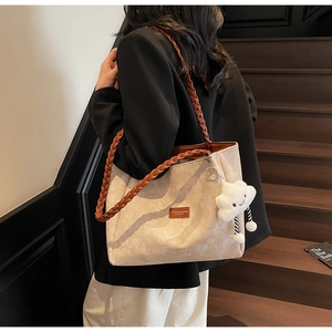 Detail of off-white tote bag with woven brown strap and a white cloud plush charm decoration
