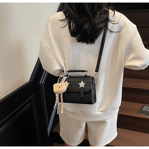 Détail du sac bandoulière en cuir grainé noir avec boucle étoile et breloque ours