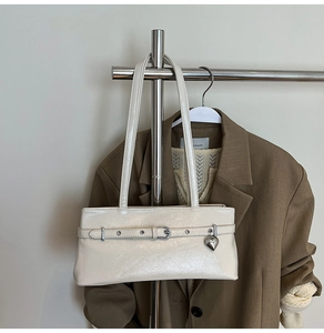 Detail of cream glossy leather shoulder bag with silver buckle and heart pendant charm