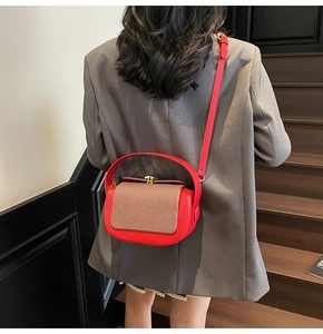 Detail of red leather and brown textured flap bag worn by a model in a modern indoor setting
