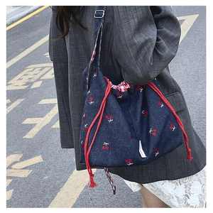 Detailed close-up of denim bucket bag with cherry embroidery and red drawstring closure