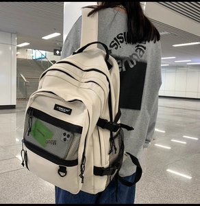 Détail d'un grand sac à dos beige avec plusieurs compartiments et une poche filet zippée
