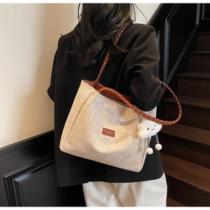 Close-up of beige jacquard tote bag with woven brown leather straps and plush charm