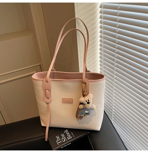 Detail of cream tote bag featuring pink straps, lychee texture, and cute bear charm