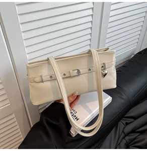 Close-up of cream underarm bag with belt buckle detail and silver heart pendant