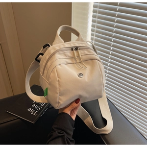 Detailed shot of cream mini nylon backpack with a round metal logo and green side label