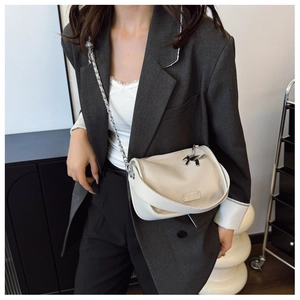 Detail of cream-colored grain leather crossbody bag with silver horse charm and metal chain