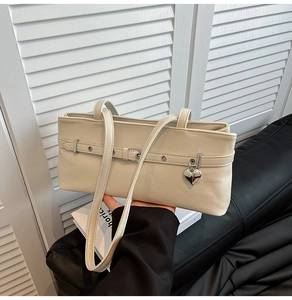 Close-up of beige underarm bag with silver heart pendant and metal eyelet belt details