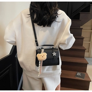 Détail du sac bandoulière en cuir noir avec logo étoile et accessoire de charme ours mignon