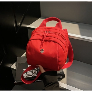 Detail of red canvas backpack with metal fashion logo and layered zipper compartments