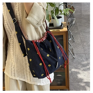 Detail of denim drawstring bag with yellow flower embroidery and red rope strap