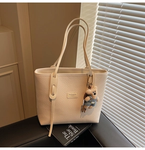 Detail of lychee pattern leather tote bag with MashaKeke logo and cute teddy bear charm