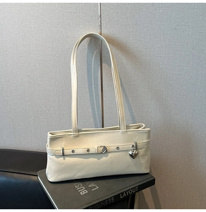 Detail of cream shoulder bag featuring adjustable buckle strap and silver heart charm pendant
