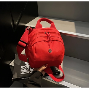 Detail of red canvas bag with multi-zipper layers and a metallic M logo on books