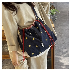 Detail of floral embroidery and red drawstring on a denim bucket shoulder bag