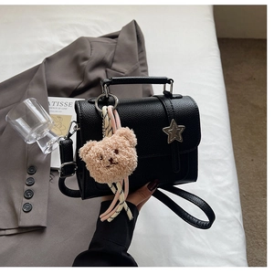 Close-up of black litchi grain handbag with star ornament and plush bear charm