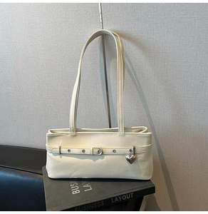 Detail of off-white faux leather baguette bag with silver heart charm and belted strap