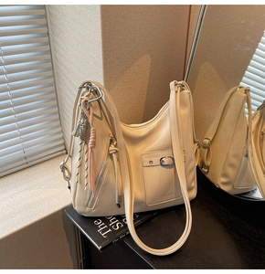 Detail of cream leather tote bag featuring feather charm and silver buckle pocket detail