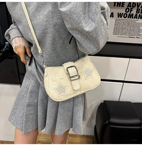 Detail of beige leather crossbody bag with star studs and silver buckle on model