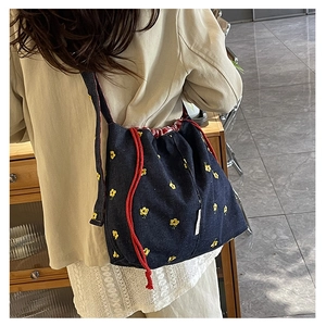 Detail of blue denim bucket bag featuring yellow floral embroidery and red drawstring cord