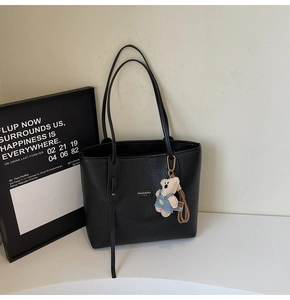 Close-up of black lychee texture tote bag with a cute bear charm and long shoulder strap