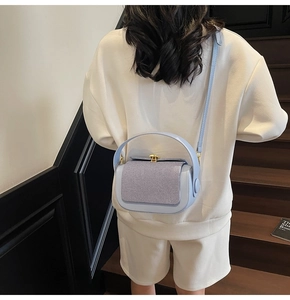 Detail of light blue crossbody pillow bag showing woven texture and gold metal buckle