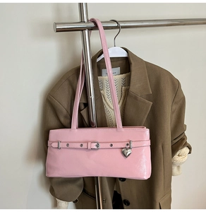 Detailed view of pink glossy leather underarm bag with heart pendant and metallic eyelets