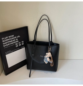 Detail of black pebbled leather tote bag with a cute bear plush keychain and metal logo tag