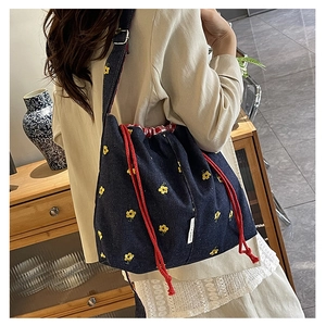 Close-up of canvas bucket bag featuring yellow flower embroidery and red drawstring cord