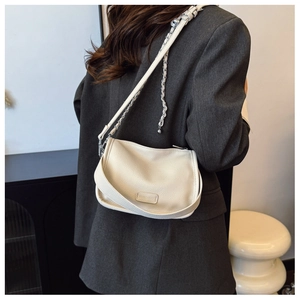 Detail of cream white pebbled leather crossbody bag with chain strap on grey blazer