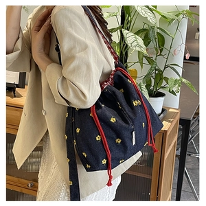 Detailed shot of denim bucket bag featuring yellow daisy embroidery and red drawstring