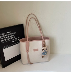 Close-up of cream tote bag with pink straps and a cute plush bear charm accessory