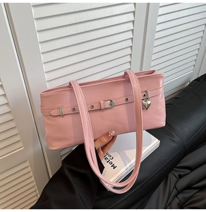 Detail of pink faux leather shoulder bag featuring metal heart pendant and strap buckle