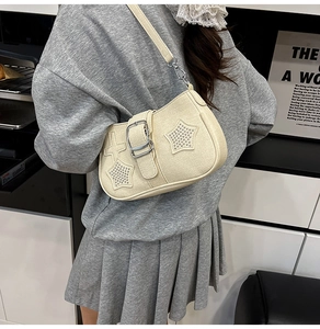 Detail view of a cream shoulder bag featuring silver star rivets and metal buckle design