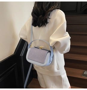 Detail showing blue pillow bag with purple woven texture on model in white sweatshirt