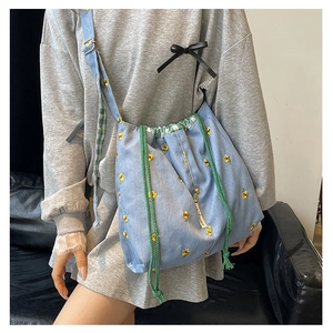 Detail of light blue denim bucket bag featuring yellow floral embroidery and drawstring