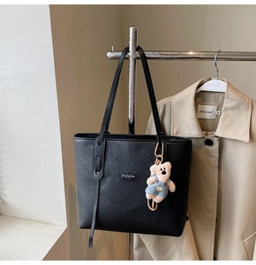 Detail of black pebbled leather tote bag with a metal logo and cute teddy bear charm