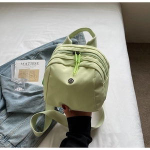 Detail of light green waterproof nylon shell bag featuring dual zippers and metal logo