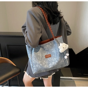 Detail of light blue denim tote bag with clover print, woven strap and cloud charm