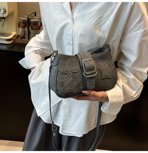 Detail of dark grey denim crossbody bag featuring metal star rivets and a cross patch design