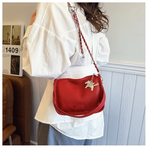 Detail of red litchi leather crossbody bag featuring metal chain and silver pegasus charm